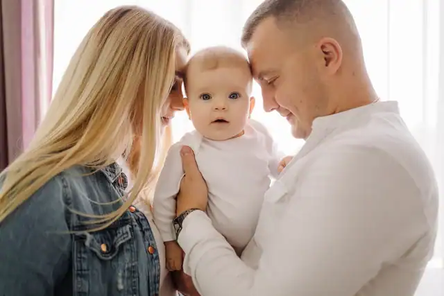 Parents holding baby indoors by window