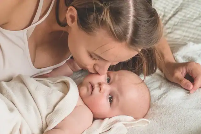 Mother kissing baby while lying on bed