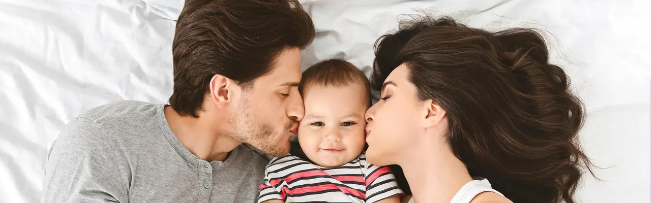 Parents kissing baby while lying on bed