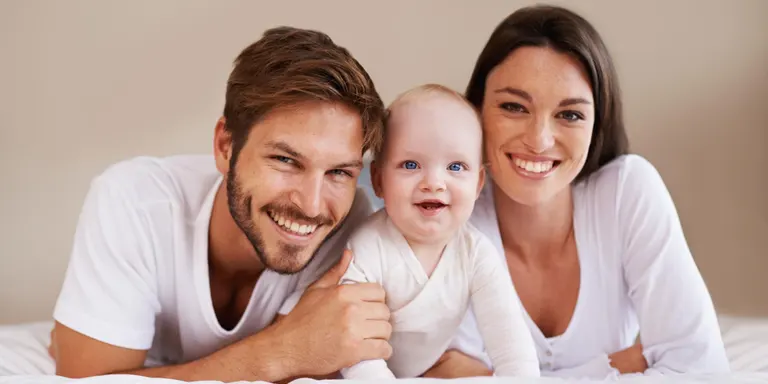 Smiling parents with baby lying on bed